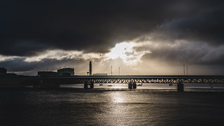 Dramatic Bridge Silhouette Over River with Sun Rays Through Clouds
