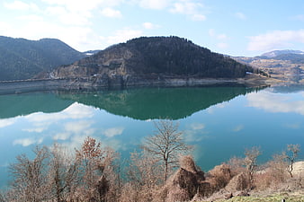 Serene turquoise lake reflecting forested mountain and dam