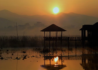 Silhouette of wooden stilt house on misty lake at sunrise
