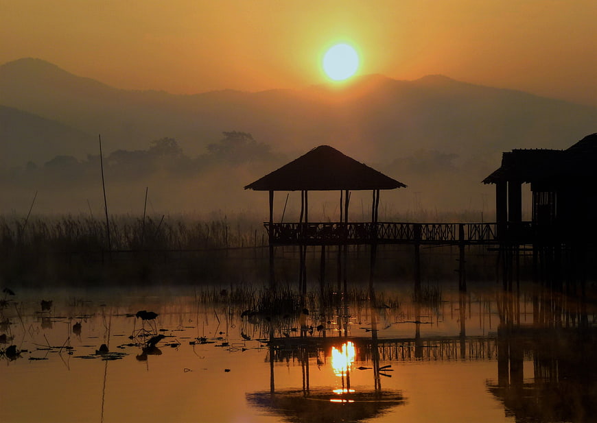 Silhouette of wooden stilt house on misty lake at sunrise