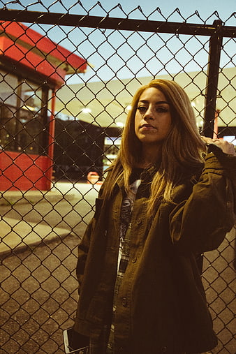 Young woman portrait behind chain link fence at dusk