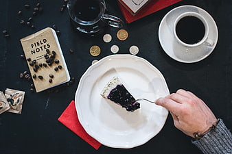 Top view of hand eating blueberry cheesecake with coffee