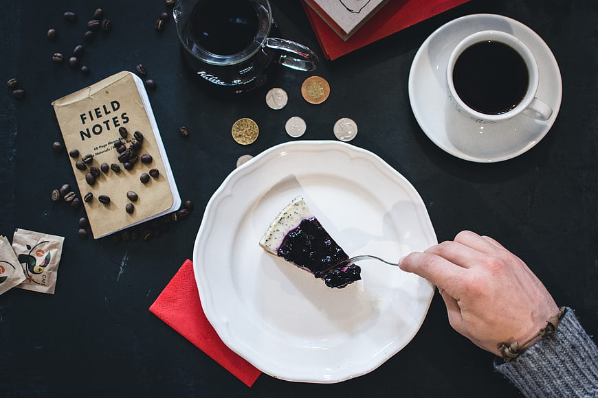 Top view of hand eating blueberry cheesecake with coffee