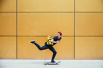 Man skateboarding with yellow backpack against orange wall