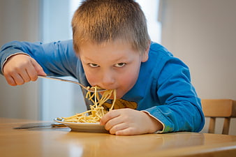 Young boy eating spaghetti with intense expression