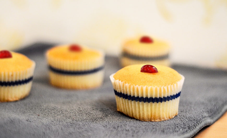 Homemade Vanilla Cupcakes with Red Cherry Topping on Gray Cloth