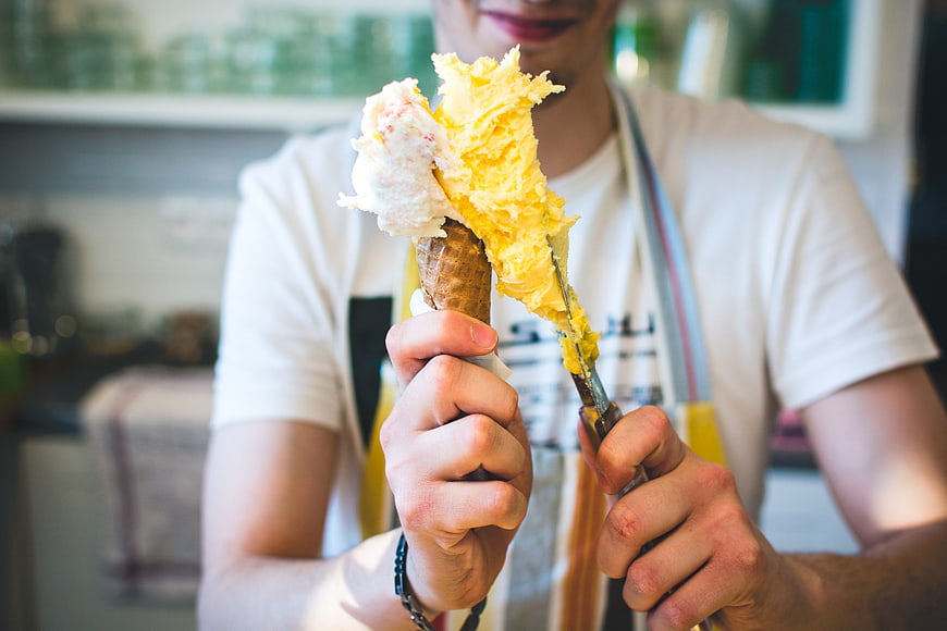 Man scooping yellow gelato into a waffle cone