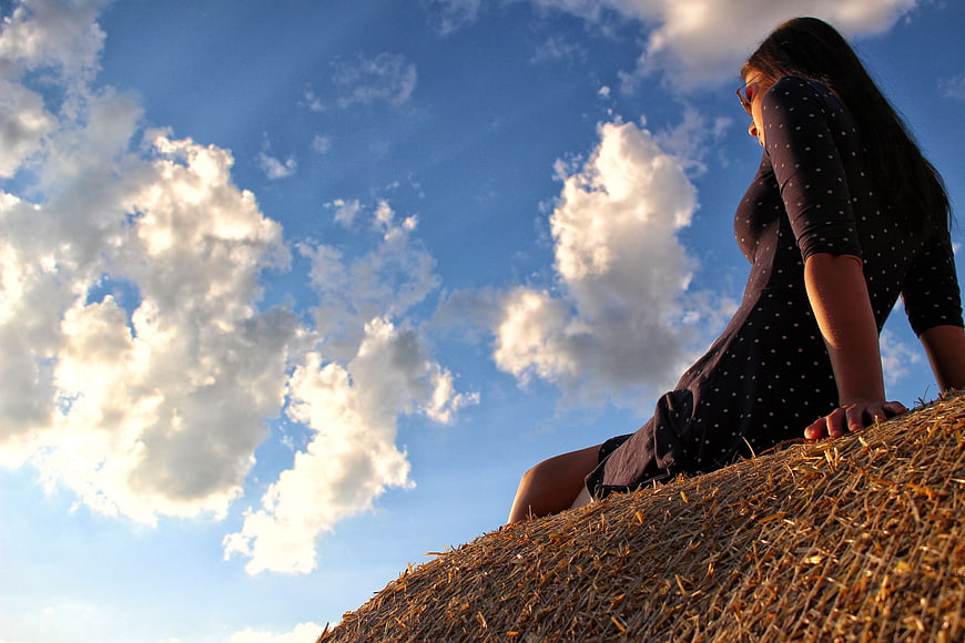 Woman Sitting on Hay Bale Against Blue Sky