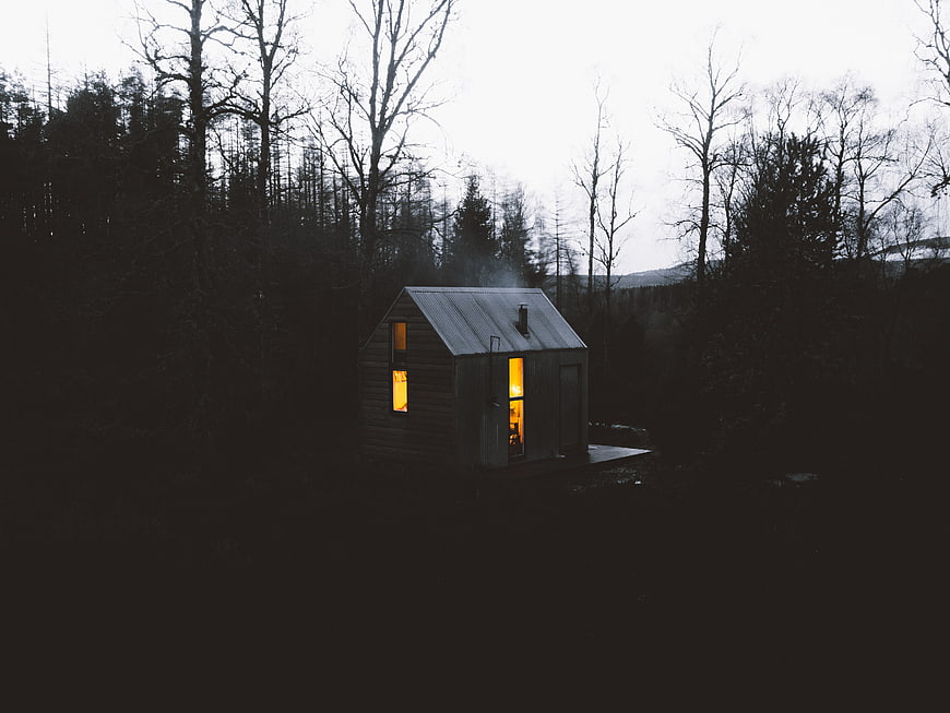 Cozy wooden cabin with warm light in dark forest at dusk