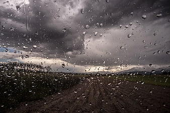 Raindrops on car windshield overlooking rural dirt road