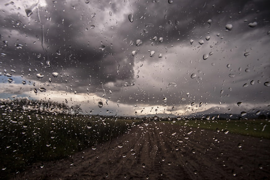 Raindrops on car windshield overlooking rural dirt road