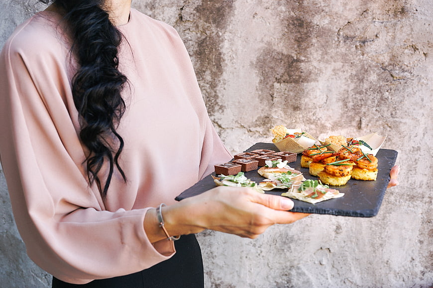 Woman holding slate platter of gourmet appetizers and desserts