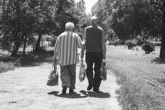 Senior couple walking away with bags on a sunny path
