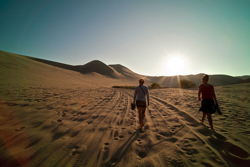 Two women walking on sand dunes at sunset