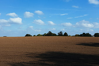Plowed brown agricultural field under blue sky with clouds