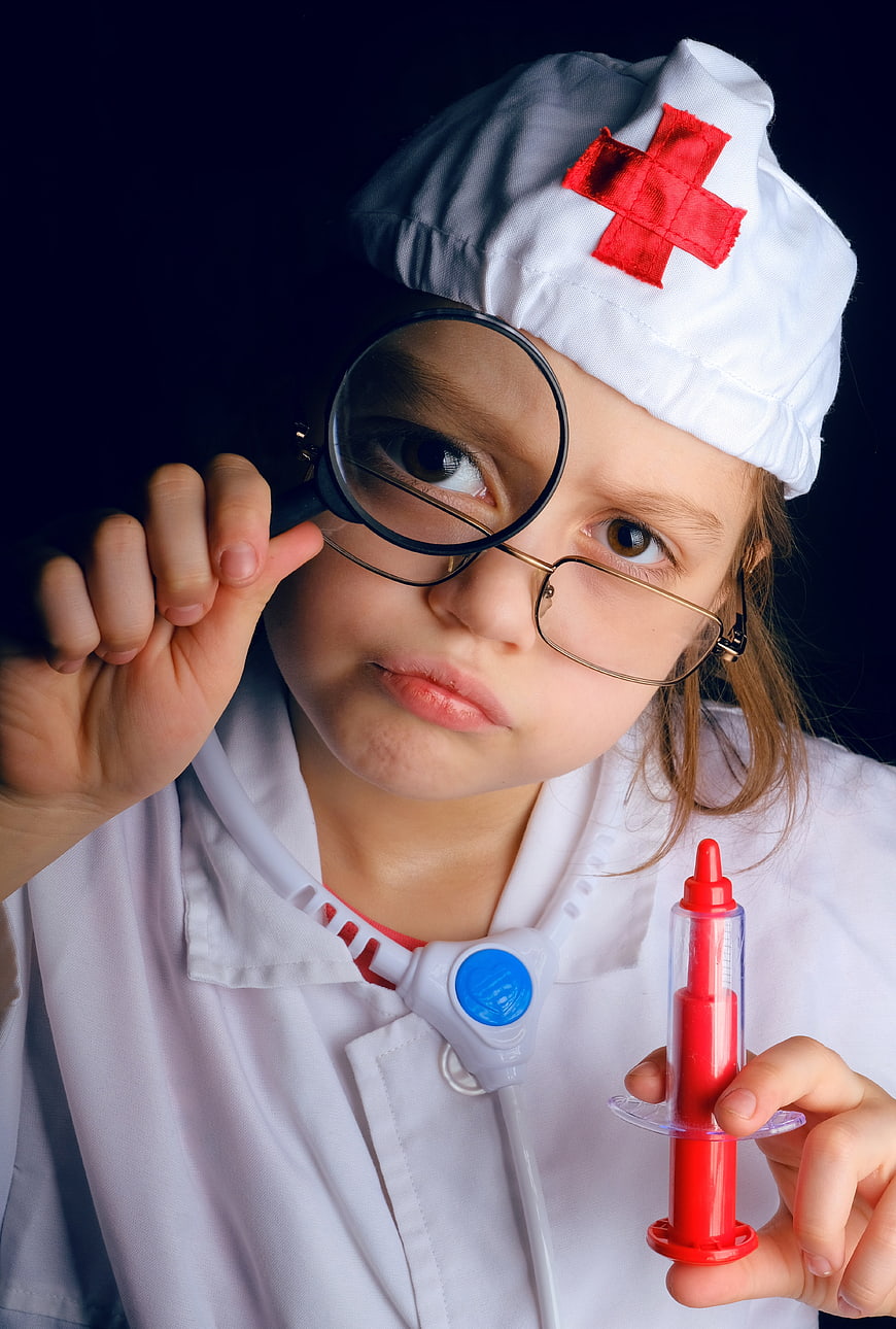 Child playing doctor with magnifying glass and toy syringe