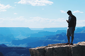Man Checking Smartphone on Canyon Cliff Edge