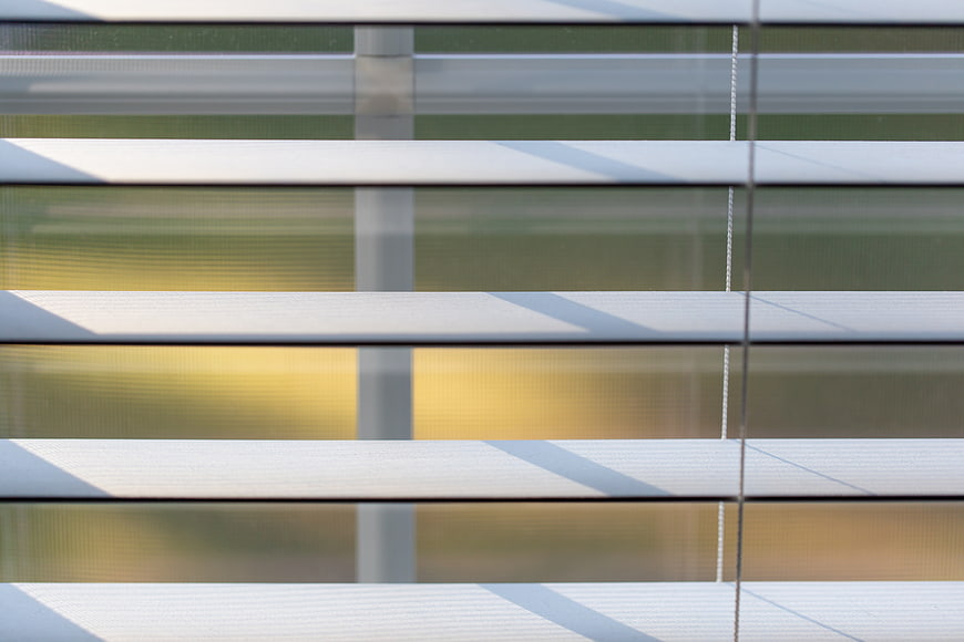 Close-up of white window blinds with sunlight and shadows