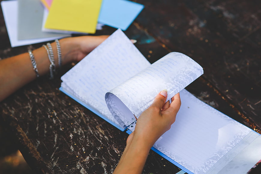 Hands turning pages of a notebook on a dark wooden table
