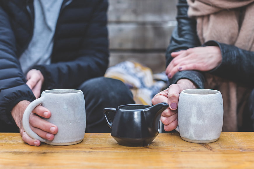 Couple holding ceramic mugs and teapot on wooden table