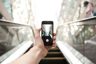 Hand holding smartphone taking photo on escalator