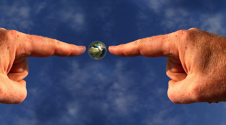 Two Hands Holding Small Earth Globe Against Blue Sky