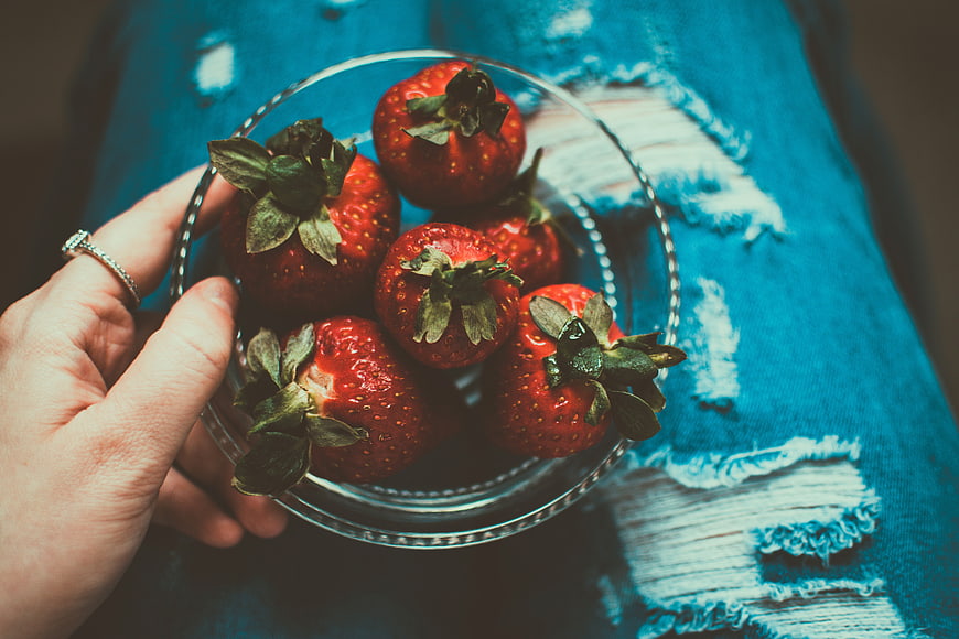 Hand holding bowl of strawberries on ripped jeans