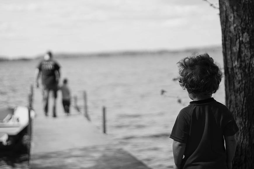 Child Watching Family on Dock by Lake in Black and White