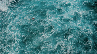 Aerial view of surfer paddling in turquoise ocean waves