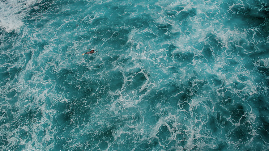 Aerial view of surfer paddling in turquoise ocean waves