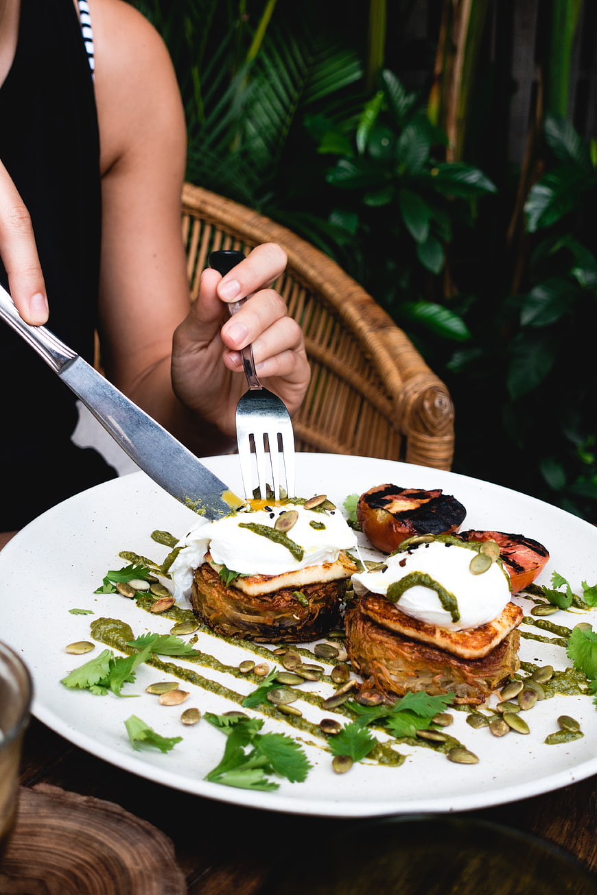 Woman cutting into brunch dish with poached eggs and hash browns