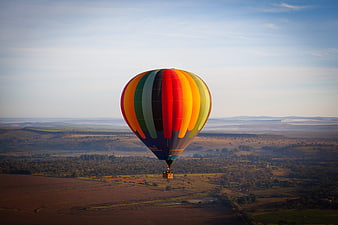 Colorful hot air balloon floating over vast rural landscape at sunrise