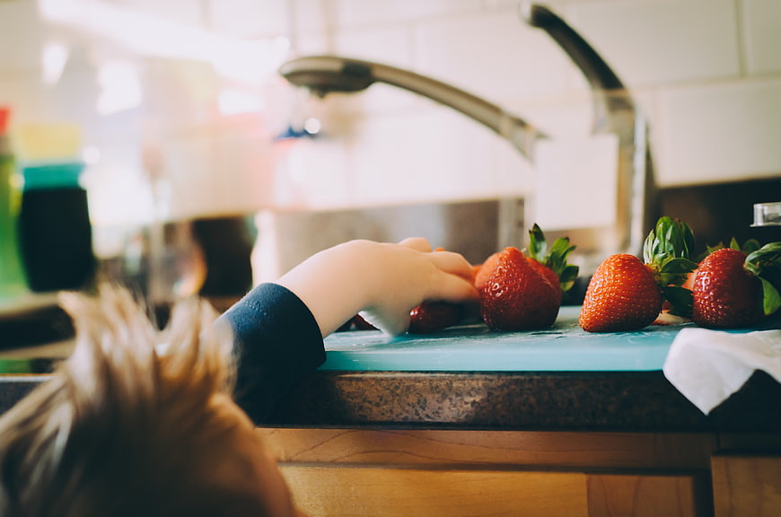 Child's Hand Reaching for Strawberries on Kitchen Counter