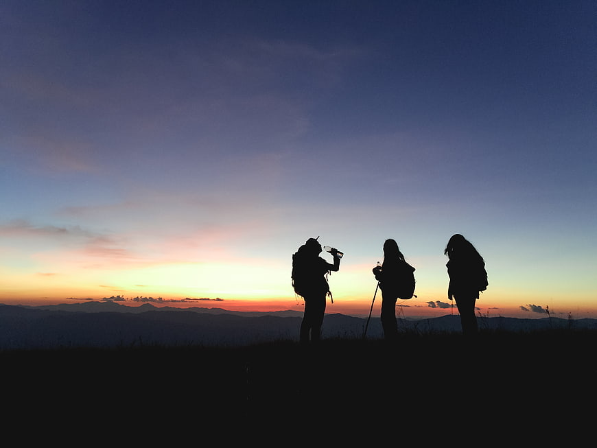 Silhouettes of Hikers on Mountain Summit at Sunset