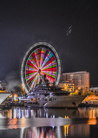 Luxury yacht docked near colorful Ferris wheel at night