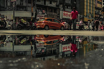 Orange car and man reflected in street puddle