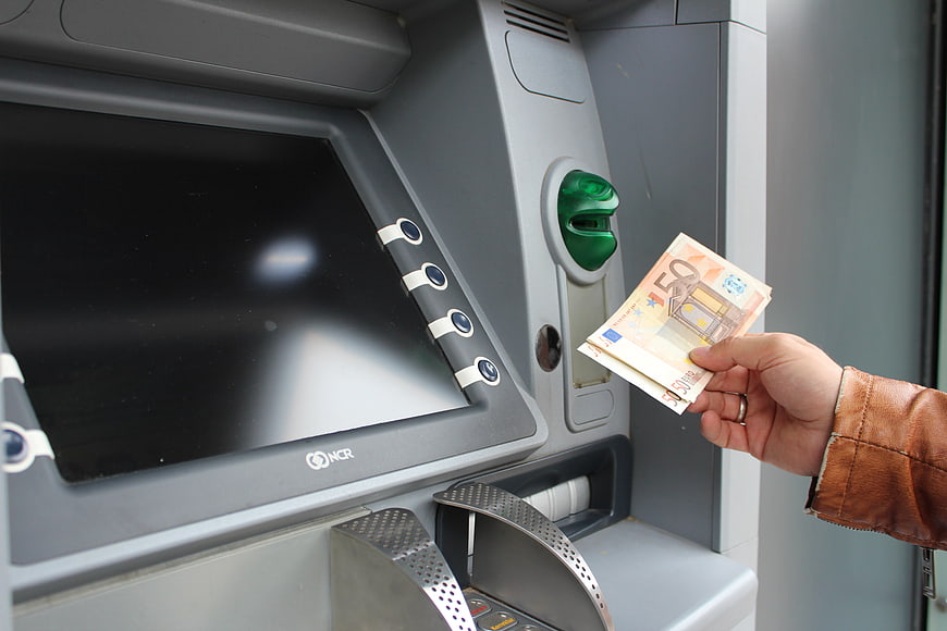 Hand holding fifty euro banknotes near ATM machine