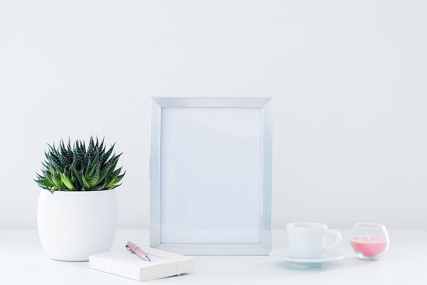 Minimalist white desk setup with succulent, notebook, and silver frame mockup