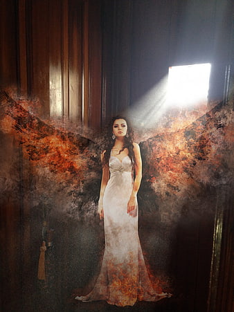 Woman with fiery wings in dark room with light beam