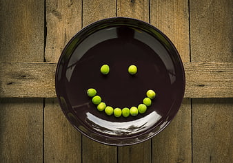 Green peas arranged as a smiley face on a dark ceramic plate