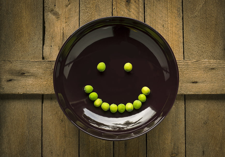 Green peas arranged as a smiley face on a dark ceramic plate