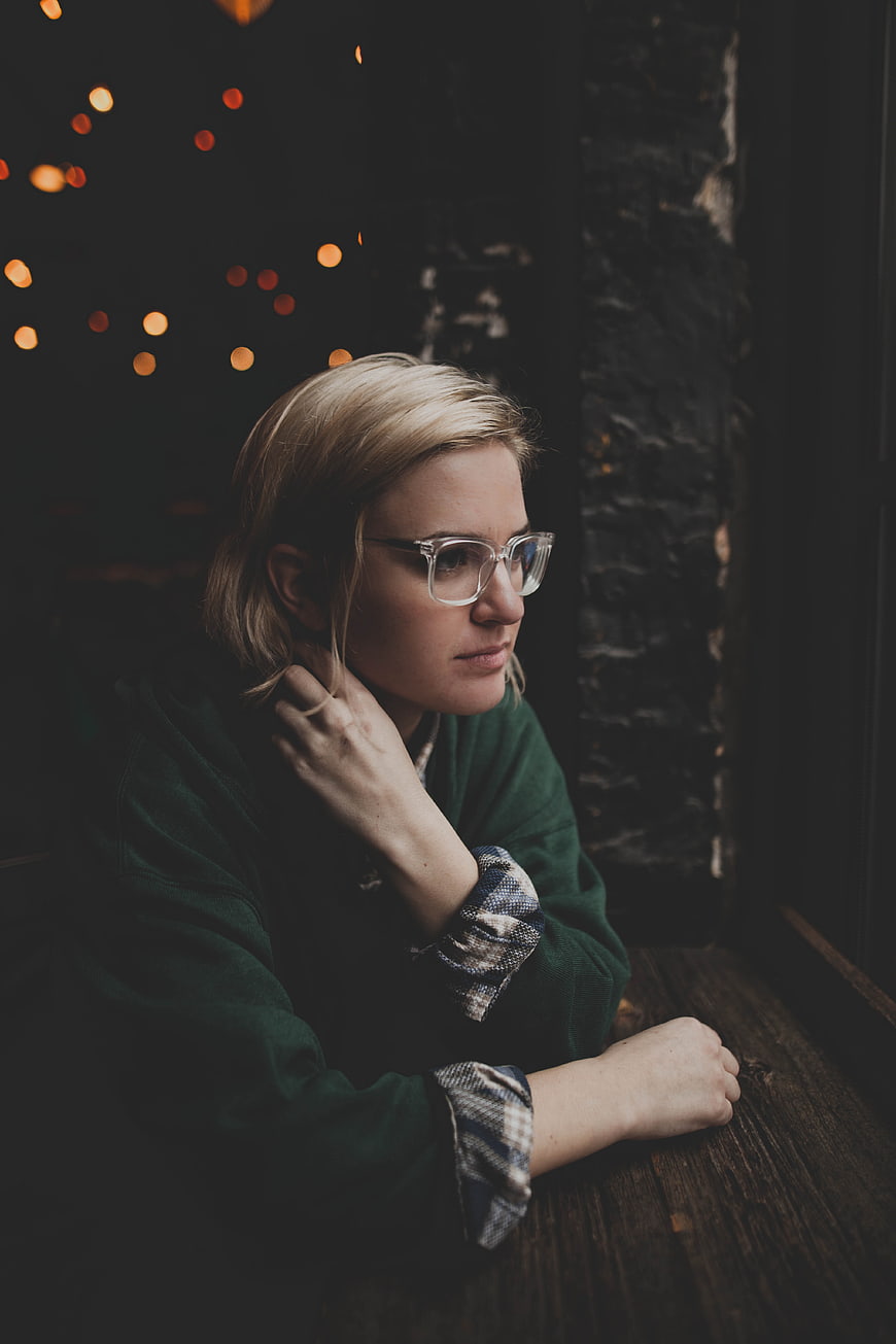 Pensive blonde woman with glasses looking out window at night