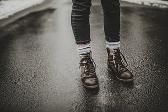 Close-up of worn leather boots on wet asphalt road