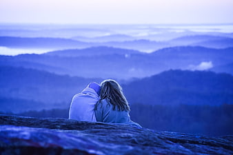 Couple wrapped in blanket overlooking blue mountain range