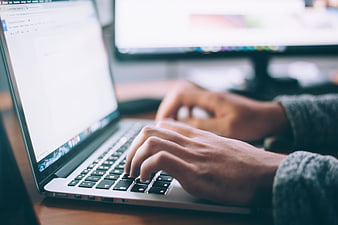 Close-up of hands typing on laptop keyboard in office