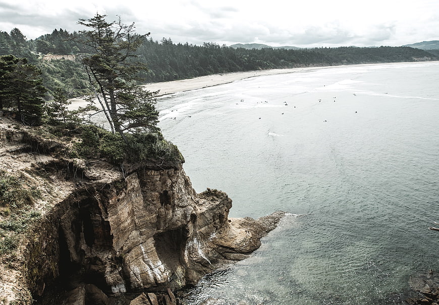 Dramatic coastal cliff overlooking sandy beach and ocean surfers