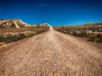 Gravel road stretching through arid desert landscape under clear blue sky