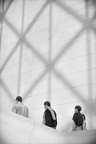 Three people walking on a modern white marble staircase with architectural shadows