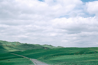 Winding Road Through Green Rolling Hills Under Cloudy Sky