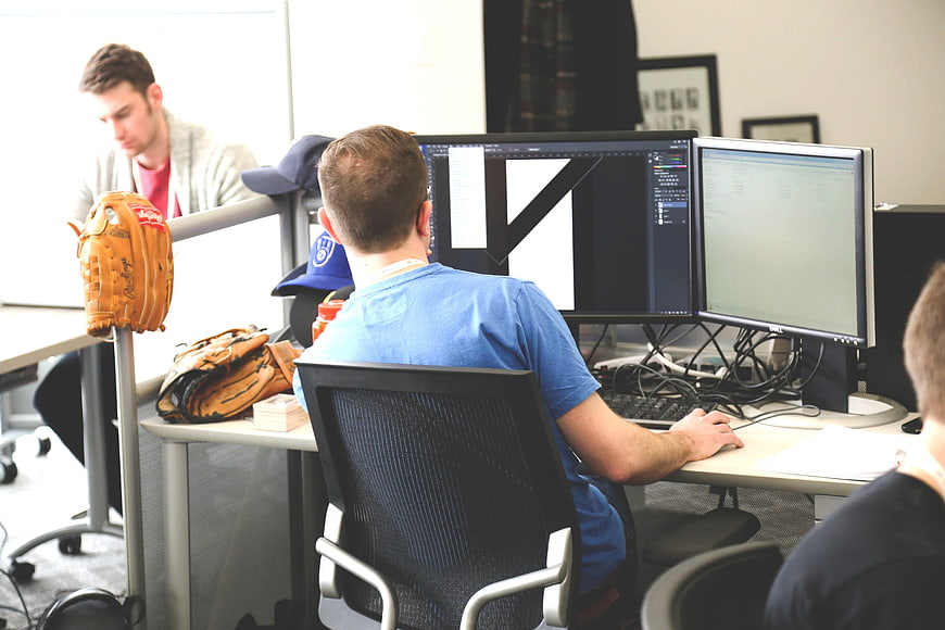 Male Graphic Designer Working On Dual Monitors In Modern Creative Office